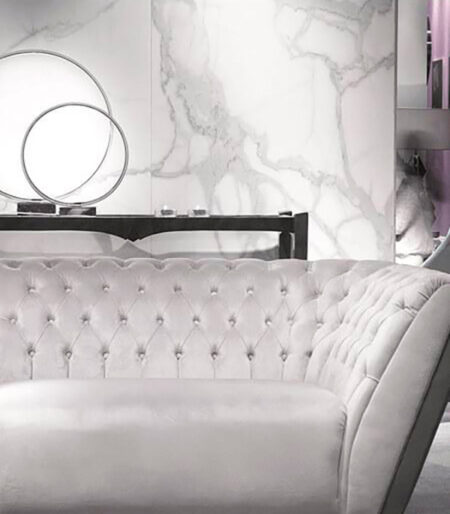 Sala de estar con sofá capitoné y pared de mármol blanco.