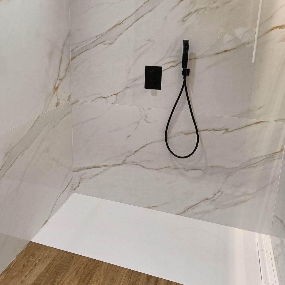 Ducha moderna con revestimientos de mármol blanco con vetas doradas, suelo cerámico efecto madera y grifería negra mate