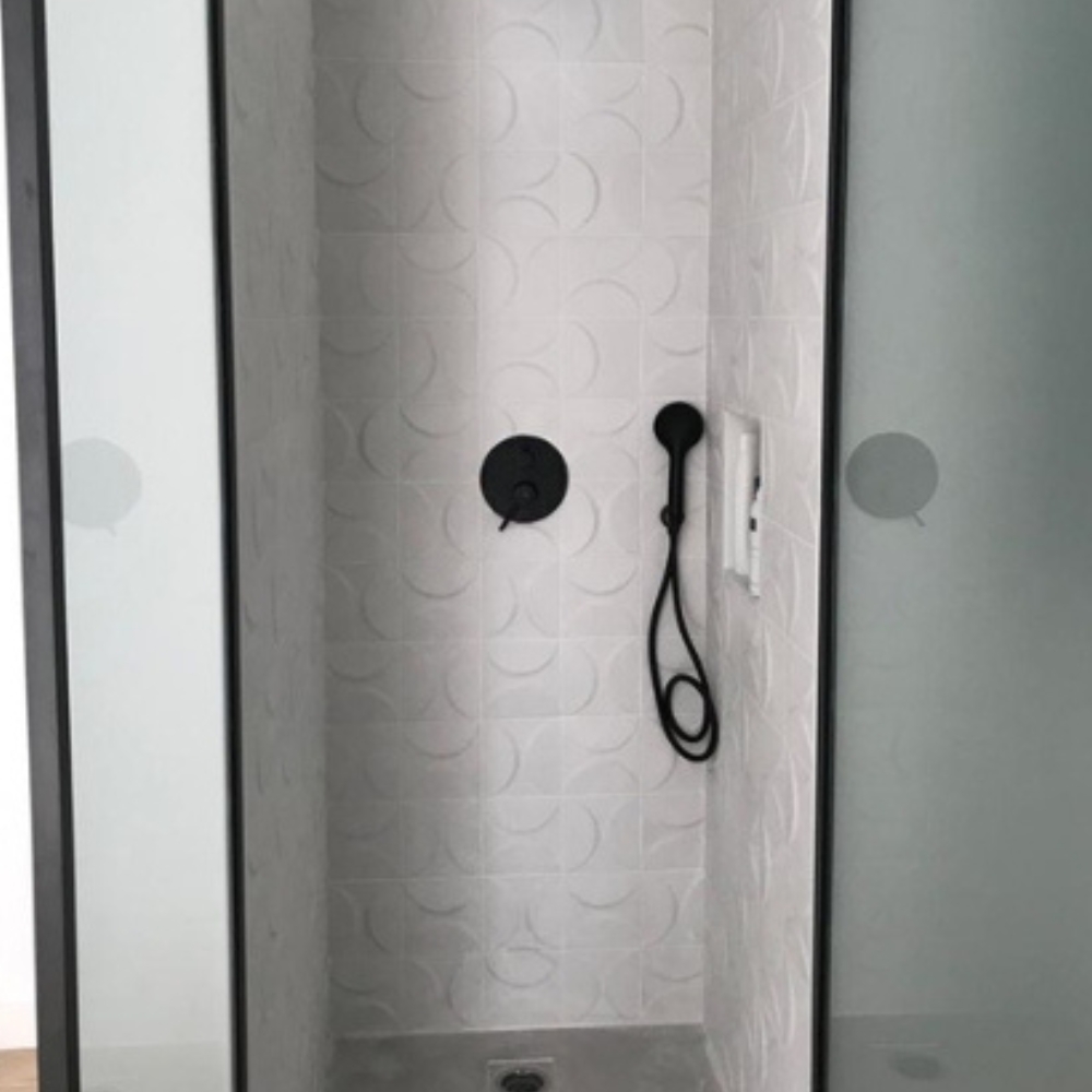 Ducha moderna con azulejos decorativos blancos en relieve, grifería negra y mamparas de cristal opaco