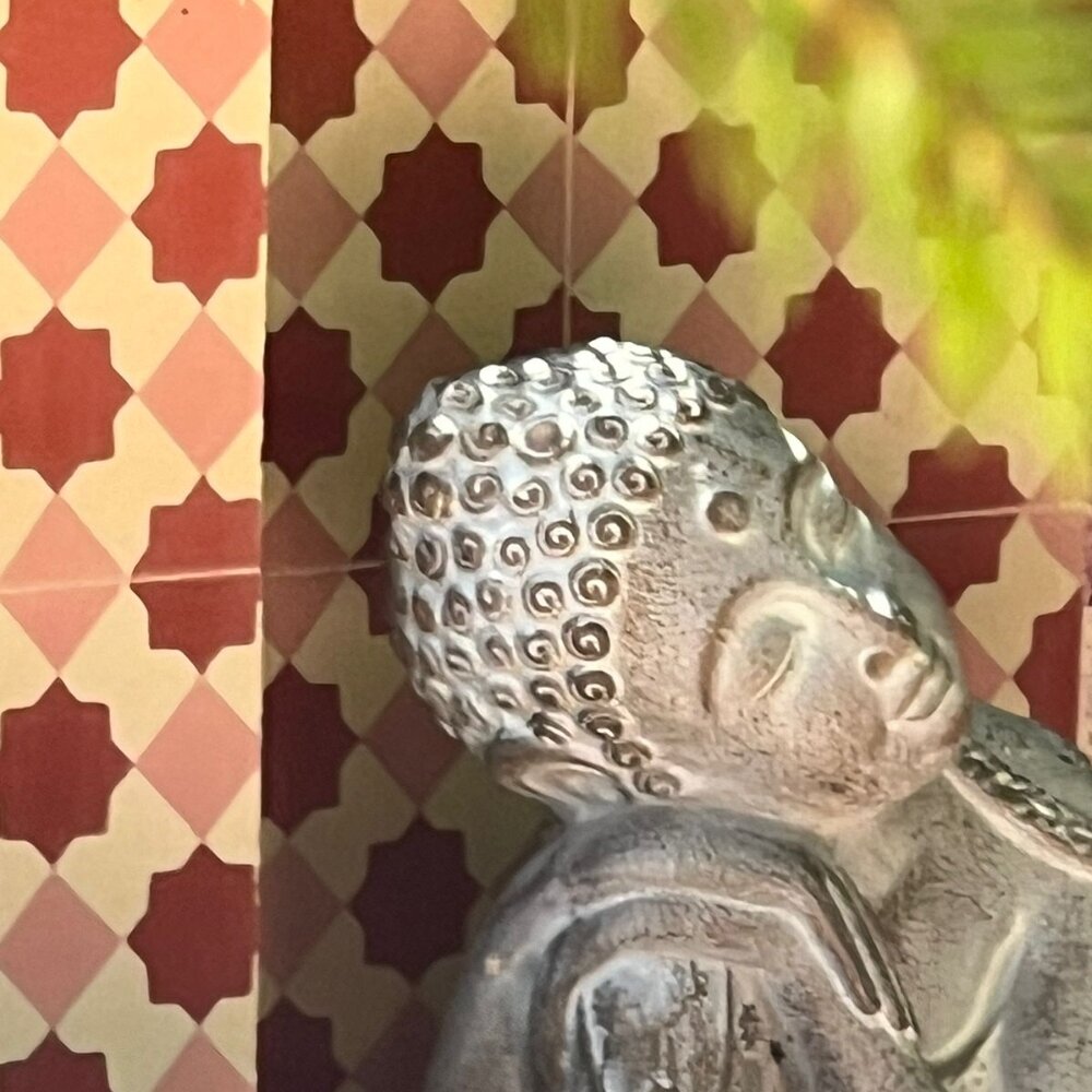 Primer plano de una estatua de Buda descansando, con fondo de azulejos geométricos en tonos rojos y blancos