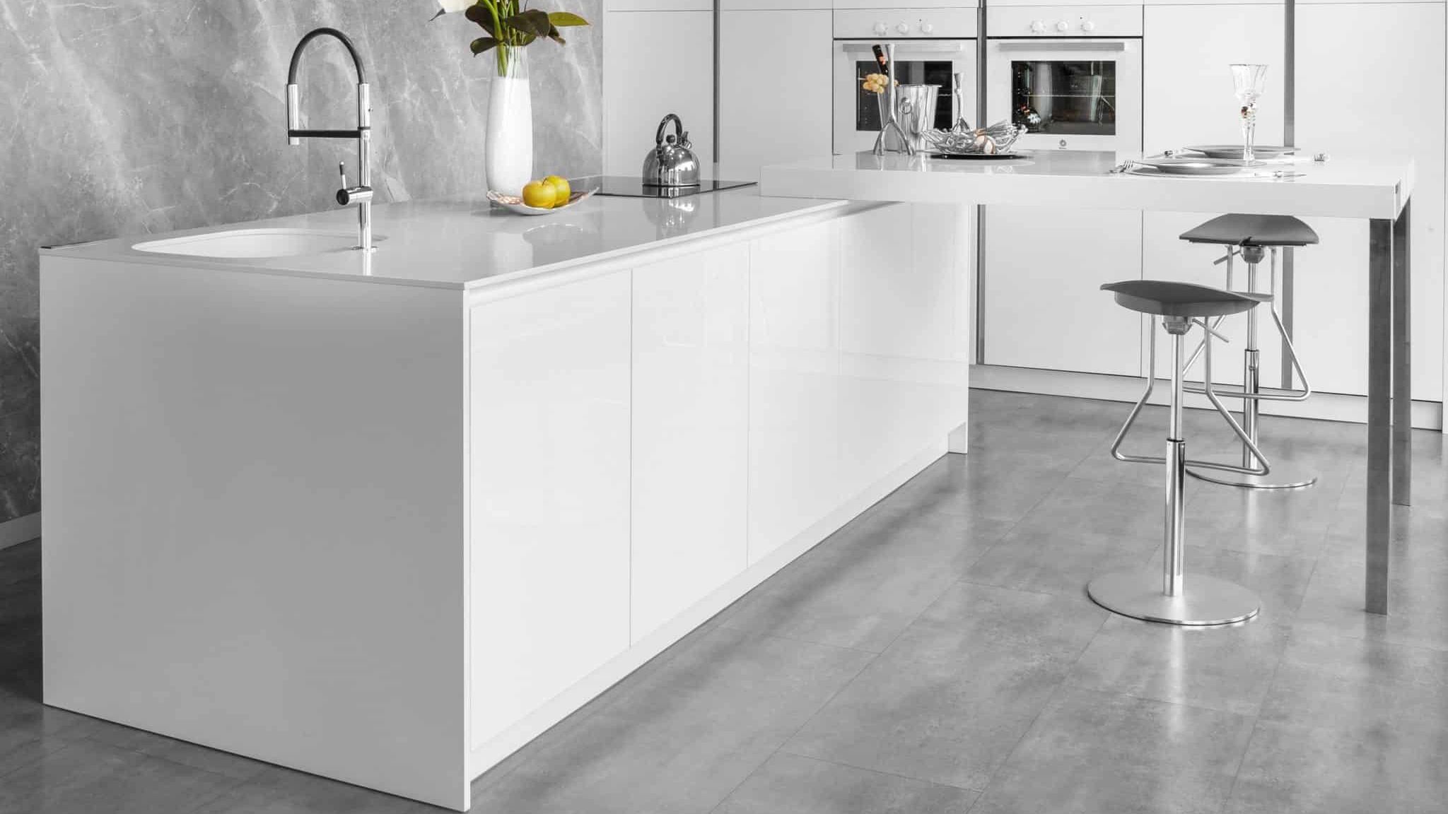 Cocina blanca con isla central, encimera minimalista, grifería moderna y taburetes metálicos