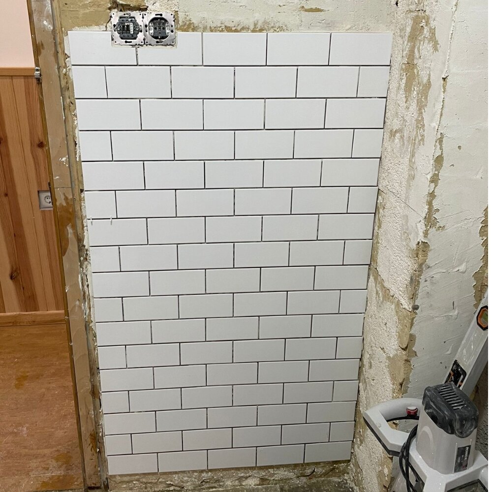 Proceso de colocación de azulejos blancos tipo metro en una pared en plena reforma.
