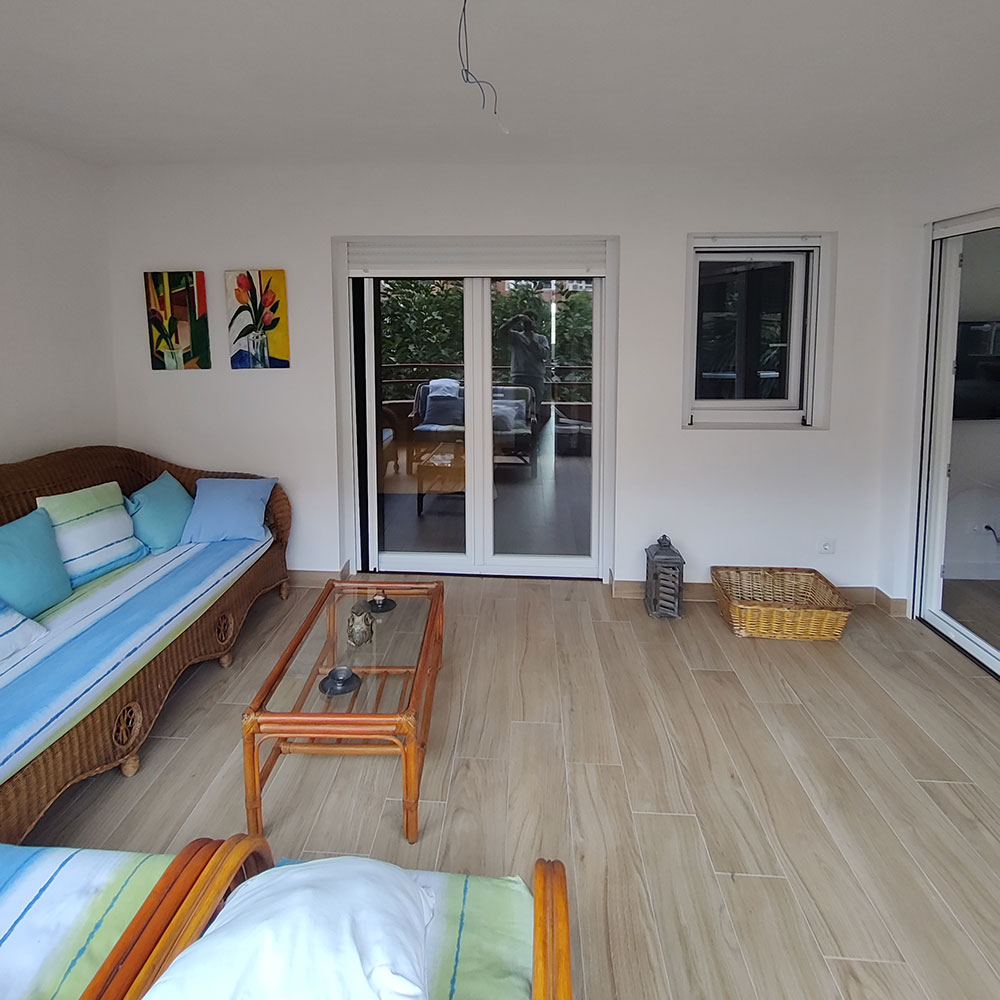 Terraza cerrada reformada con suelo cerámico imitación madera, sofás de mimbre y ventanales en Alicante