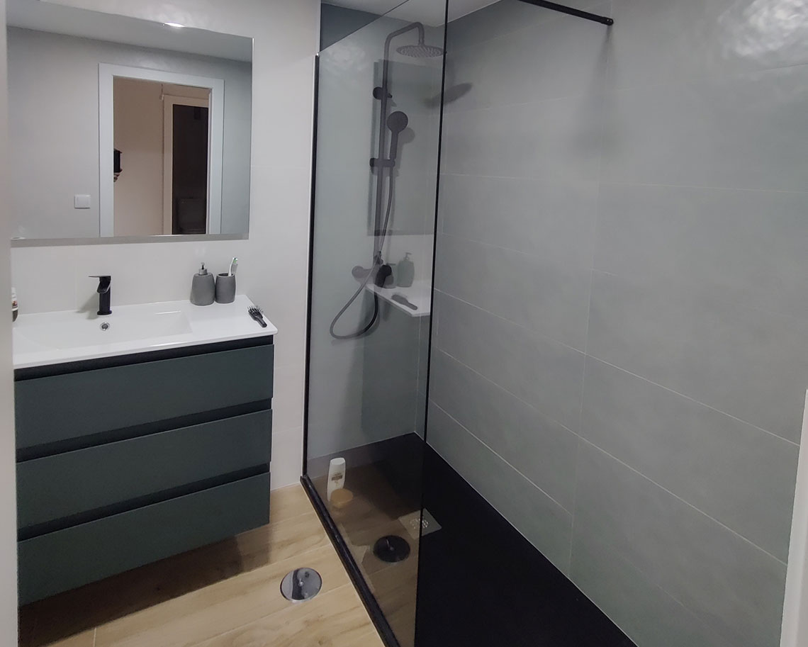 Cuarto de baño reformado con ducha italiana, muebles modernos y suelo efecto madera en Alicante