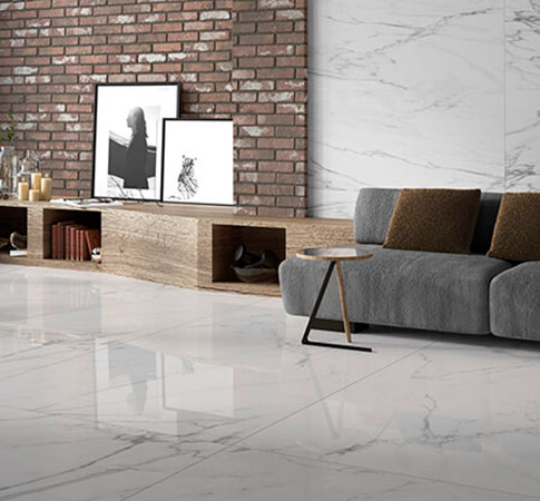 Pavimento porcelánico imitación mármol blanco en salón con pared de ladrillo y sofá gris