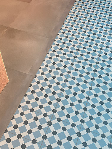 Suelo de pavimento porcelánico con baldosas geométricas en tonos blanco y azul combinadas con losas lisas beige