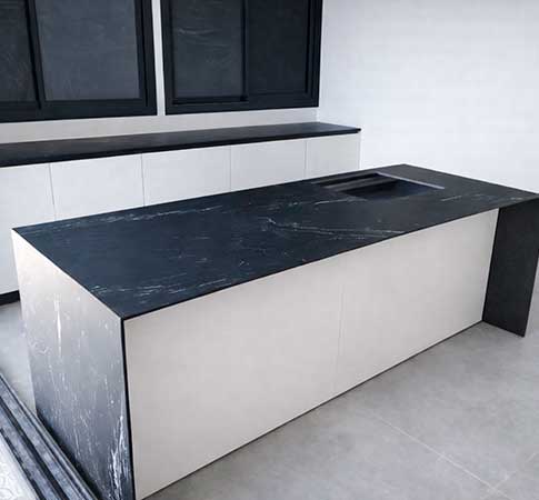 Isla de cocina con encimera negra efecto mármol sobre pared blanca lisa