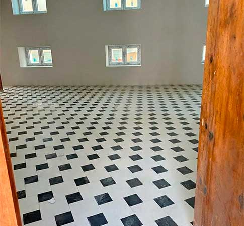 Vista del interior de una habitación recién reformada con suelo de baldosas blancas y negras en patrón de ajedrez, paredes lisas blancas y ventanas nuevas.