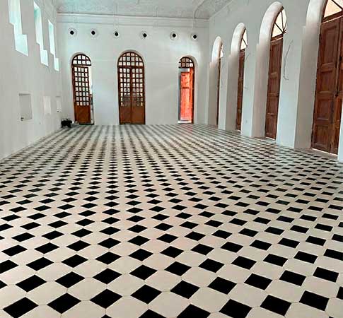 Gran salón restaurado con suelo de baldosas tipo damero en blanco y negro, paredes lisas y grandes puertas de madera con arcos.