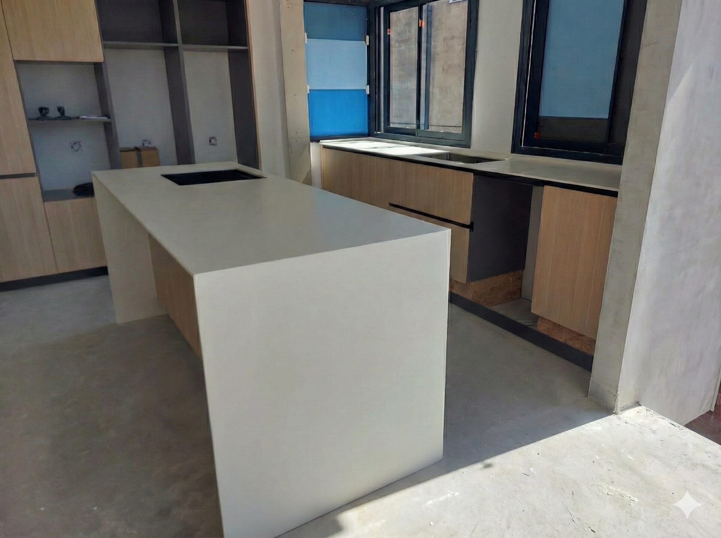 Isla de cocina moderna de color blanco con muebles de madera clara, fregadero negro y suelo continuo de cemento gris.