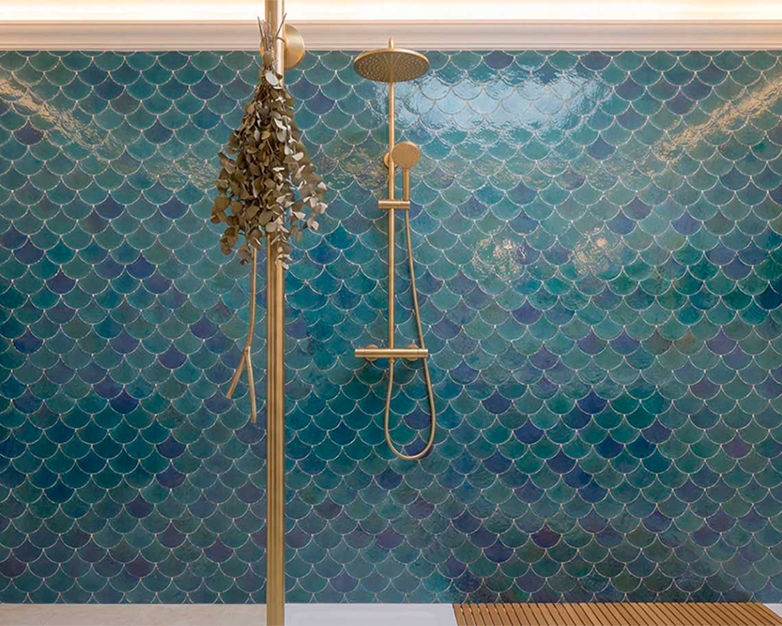 Revestimiento de ducha con azulejos cerámicos tipo escama de pez zafiro y esmeralda, diseño de baño spa con accesorios dorados."