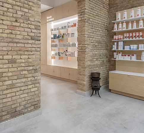 Expositor de productos en farmacia con paredes de ladrillo visto y mobiliario de madera clara