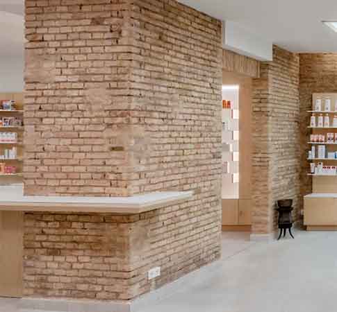 Diseño interior de farmacia con pilares de ladrillo visto, mostrador y estanterías de productos