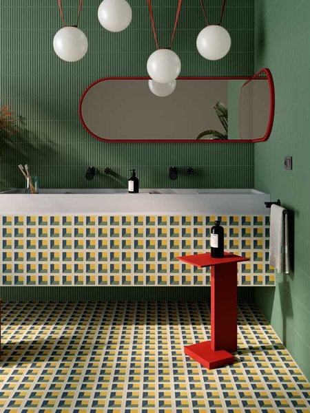 Baño con azulejos Maluhia, paredes verdes, mueble blanco, espejo rojo y suelo geométrico amarillo y azul