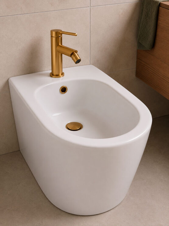 Grifo monomando para bidé en acabado dorado cepillado instalado sobre bidé de cerámica blanca con desagüe a juego en baño moderno.