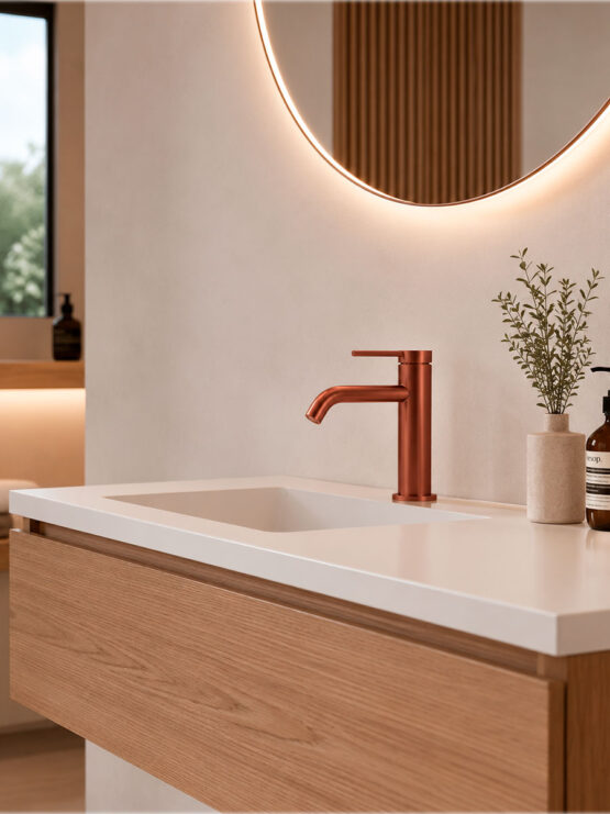 Grifo de lavabo monomando en acabado cobre cepillado instalado sobre mueble de baño suspendido de madera con lavabo blanco.